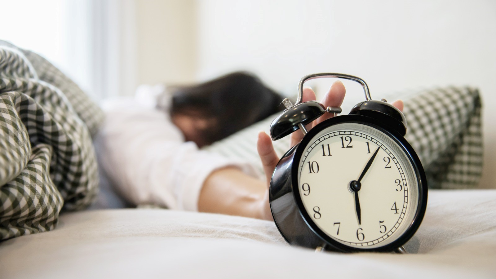 Mujer somnolienta alcanza el despertador a las 5h de la mañana tratando de apagarlo